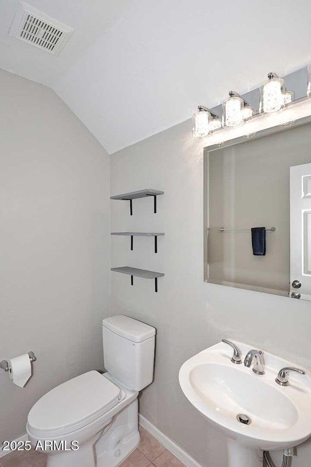 half bath featuring visible vents, toilet, tile patterned floors, vaulted ceiling, and a sink