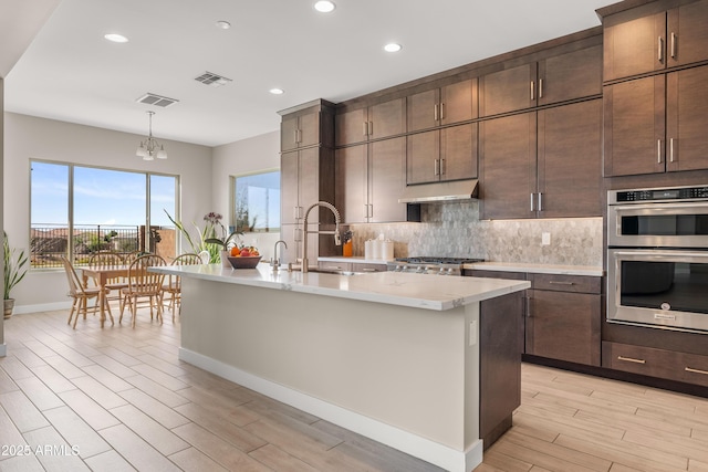 kitchen with visible vents, under cabinet range hood, a sink, backsplash, and stainless steel double oven