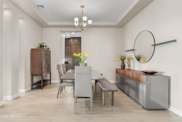 dining space with a raised ceiling, a notable chandelier, visible vents, and light wood-type flooring