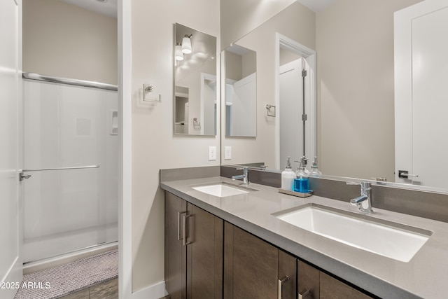 full bath with double vanity, a shower stall, baseboards, and a sink