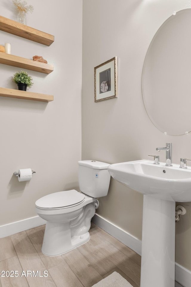 bathroom with toilet, baseboards, and wood finished floors