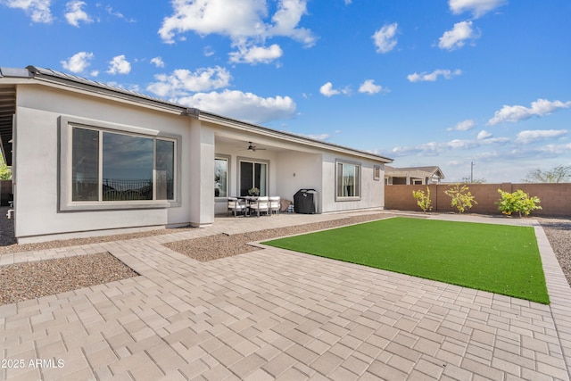 rear view of property featuring stucco siding, a fenced backyard, solar panels, ceiling fan, and a patio area