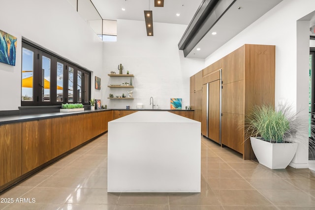 kitchen featuring a sink, built in refrigerator, light tile patterned floors, brown cabinets, and open shelves