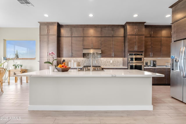 kitchen featuring visible vents, under cabinet range hood, tasteful backsplash, stainless steel appliances, and dark brown cabinets