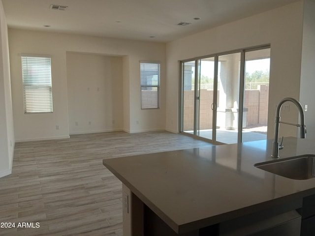 kitchen featuring a center island with sink, sink, and light wood-type flooring