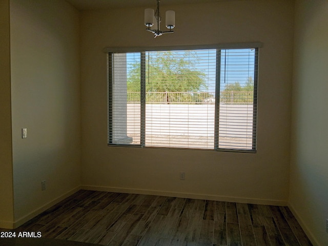 spare room with dark hardwood / wood-style flooring and an inviting chandelier