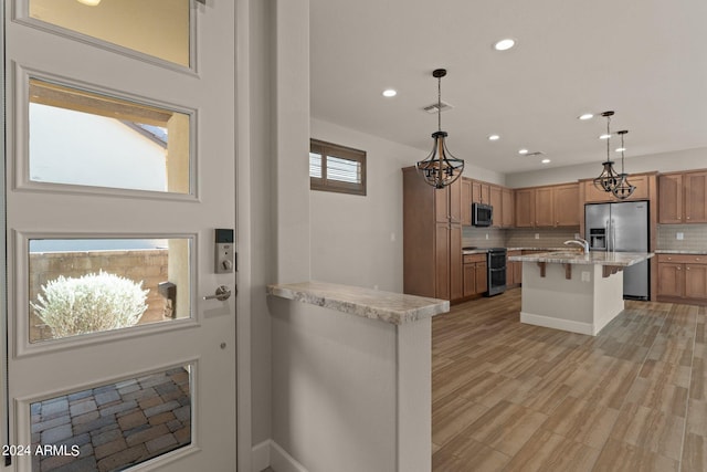 kitchen with a kitchen bar, appliances with stainless steel finishes, backsplash, light stone counters, and decorative light fixtures