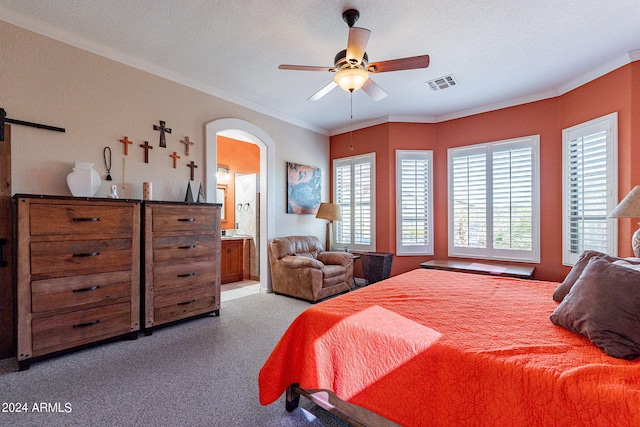 carpeted bedroom with arched walkways, ensuite bathroom, a barn door, visible vents, and ornamental molding