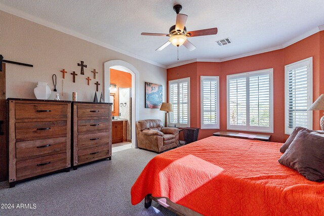 bedroom featuring visible vents, crown molding, arched walkways, a barn door, and ensuite bathroom