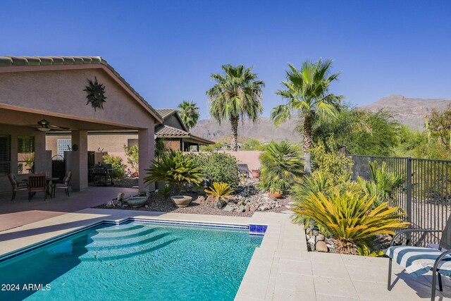 view of swimming pool with fence, a fenced in pool, a mountain view, a ceiling fan, and a patio