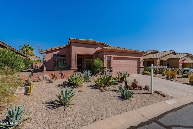 mediterranean / spanish home featuring driveway, a garage, stone siding, a tile roof, and stucco siding