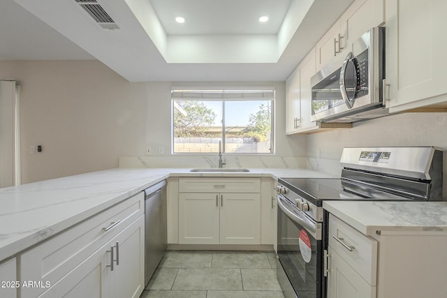 kitchen with a tray ceiling, visible vents, appliances with stainless steel finishes, a sink, and light stone countertops