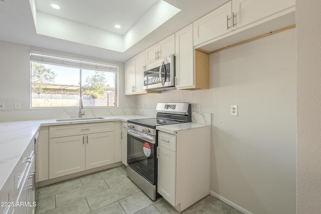 kitchen with light tile patterned floors, stainless steel appliances, a sink, white cabinets, and a raised ceiling