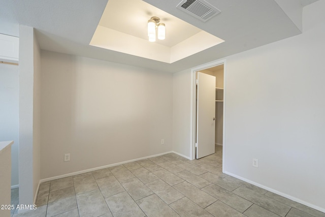 empty room with a tray ceiling, visible vents, baseboards, and light tile patterned floors