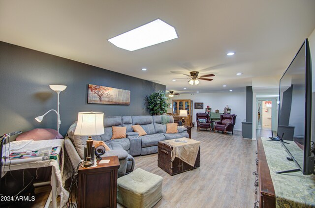 living room featuring light hardwood / wood-style floors, a skylight, and ceiling fan