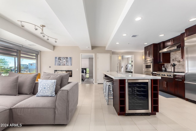 kitchen featuring sink, stainless steel appliances, beverage cooler, tasteful backsplash, and a kitchen island with sink