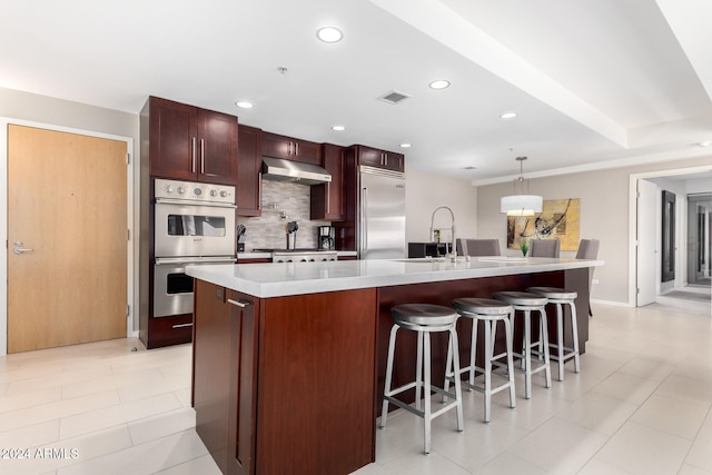 kitchen featuring sink, an island with sink, pendant lighting, decorative backsplash, and appliances with stainless steel finishes