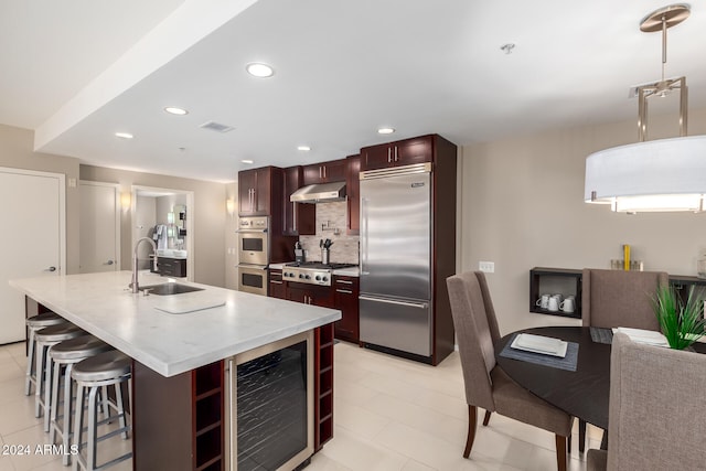 kitchen with a kitchen island with sink, sink, a kitchen bar, stainless steel appliances, and beverage cooler