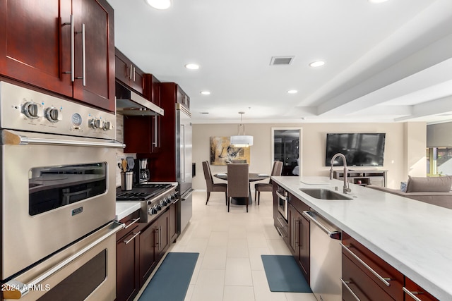 kitchen featuring light stone counters, ventilation hood, stainless steel appliances, sink, and hanging light fixtures