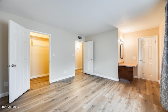 unfurnished bedroom featuring a walk in closet and light hardwood / wood-style flooring