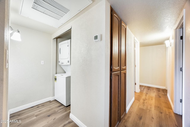 hall featuring a textured ceiling, stacked washer / drying machine, and light hardwood / wood-style floors