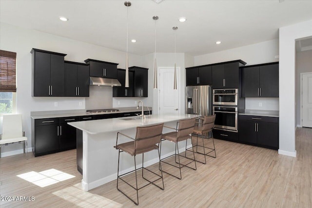 kitchen with a kitchen breakfast bar, stainless steel appliances, hanging light fixtures, and an island with sink