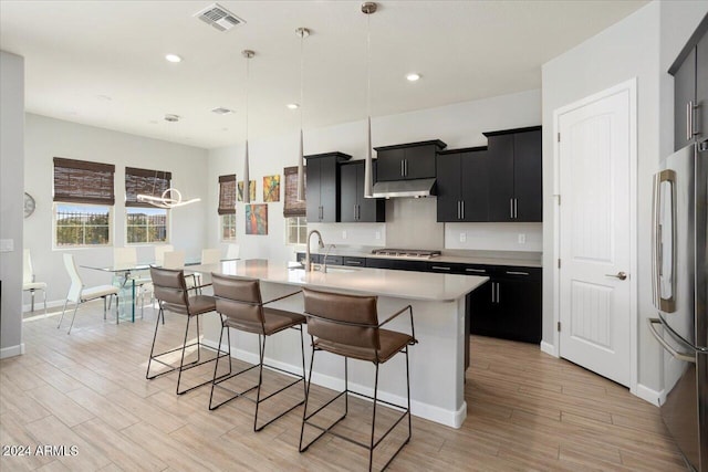 kitchen with stainless steel appliances, sink, decorative light fixtures, a center island with sink, and light hardwood / wood-style floors