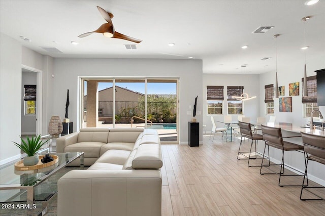 living room with ceiling fan, sink, and light wood-type flooring