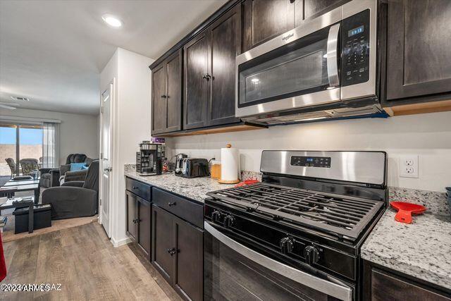 kitchen featuring light wood-type flooring, light stone counters, appliances with stainless steel finishes, and dark brown cabinetry