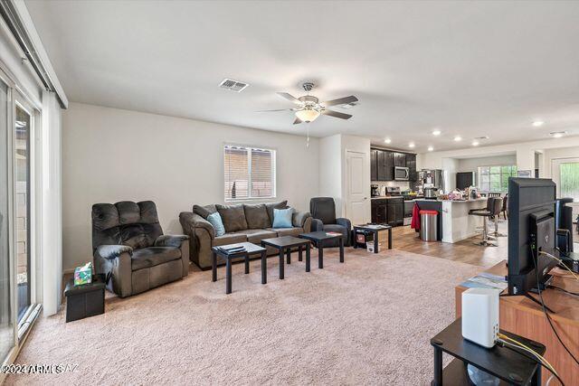 living room with ceiling fan, light colored carpet, and a wood stove