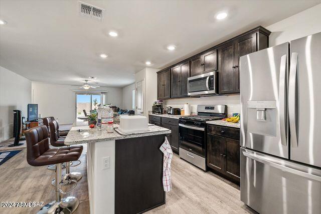 kitchen featuring ceiling fan, light hardwood / wood-style flooring, a kitchen island, a kitchen bar, and stainless steel appliances