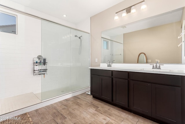 full bathroom with double vanity, a sink, walk in shower, and wood finished floors