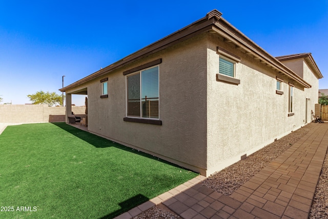 view of side of home with a fenced backyard, stucco siding, and a yard