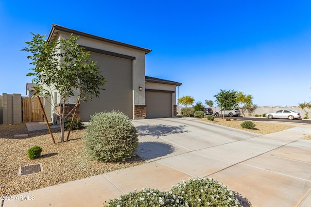 view of side of home with a gate, a garage, concrete driveway, stone siding, and stucco siding
