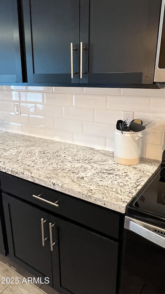 interior details featuring decorative backsplash, black / electric stove, light stone counters, stainless steel microwave, and dark cabinetry