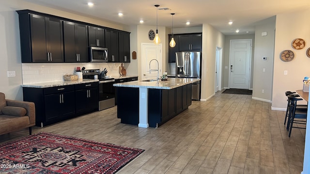 kitchen featuring light stone countertops, appliances with stainless steel finishes, a sink, light wood-style floors, and dark cabinetry