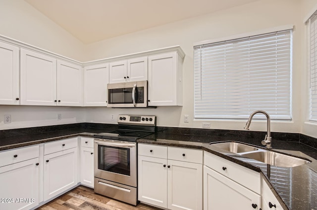 kitchen with sink, appliances with stainless steel finishes, dark stone counters, light hardwood / wood-style floors, and white cabinets