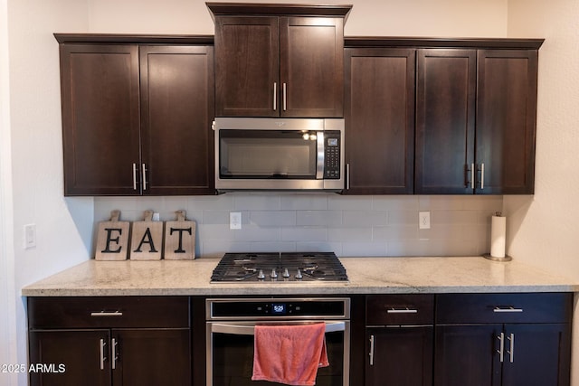 kitchen featuring stainless steel appliances, light stone countertops, tasteful backsplash, and dark brown cabinetry