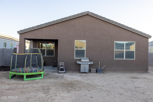 back of house featuring stucco siding, a trampoline, and fence