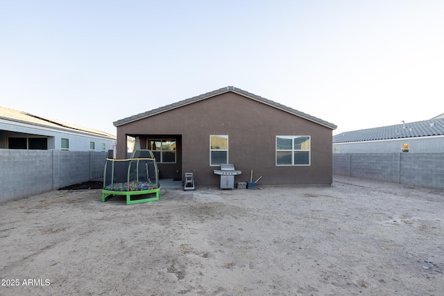 rear view of house featuring stucco siding, a trampoline, and a fenced backyard