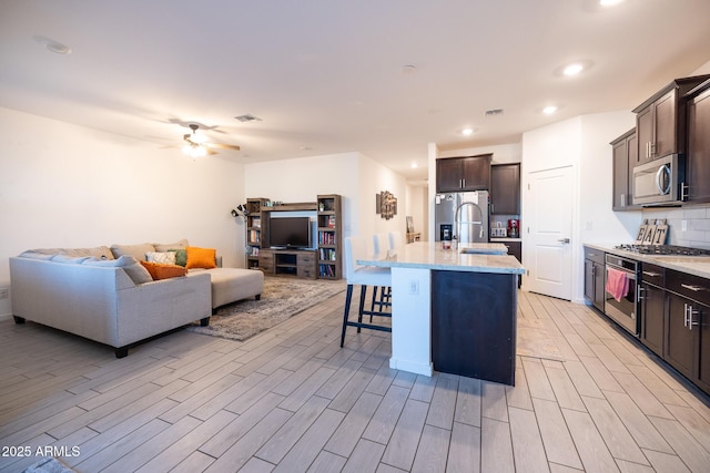 kitchen featuring a kitchen breakfast bar, open floor plan, light wood-style floors, appliances with stainless steel finishes, and decorative backsplash