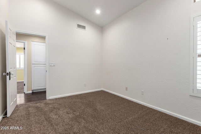 spare room with dark carpet, healthy amount of natural light, baseboards, and lofted ceiling