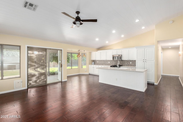 kitchen with stainless steel microwave, a sink, light countertops, lofted ceiling, and a kitchen island with sink