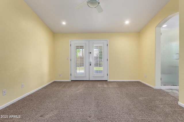 empty room featuring a ceiling fan, arched walkways, carpet floors, french doors, and baseboards