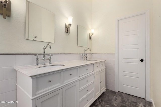 full bath featuring tile walls, marble finish flooring, double vanity, and a wainscoted wall