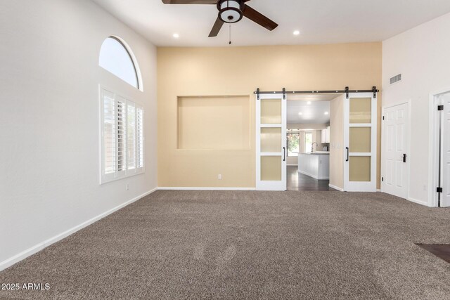 unfurnished bedroom featuring carpet flooring, a barn door, baseboards, recessed lighting, and a towering ceiling