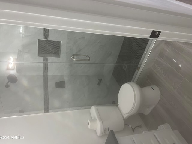 bathroom with toilet, a shower with door, and tile walls