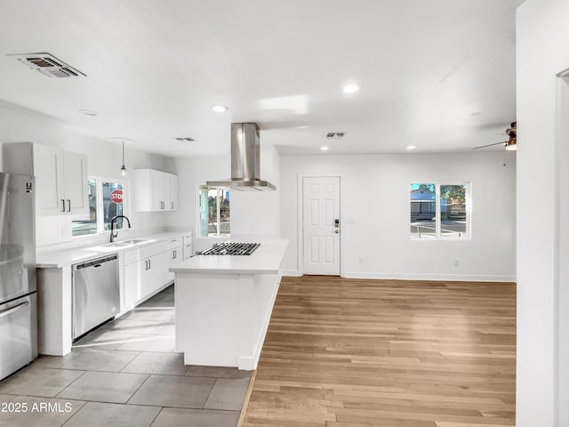 kitchen featuring white cabinets, sink, range hood, appliances with stainless steel finishes, and a kitchen island