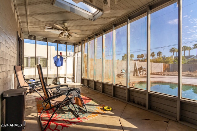 unfurnished sunroom with ceiling fan, a healthy amount of sunlight, and a skylight