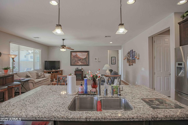 kitchen with open floor plan, an island with sink, stainless steel refrigerator with ice dispenser, and a sink